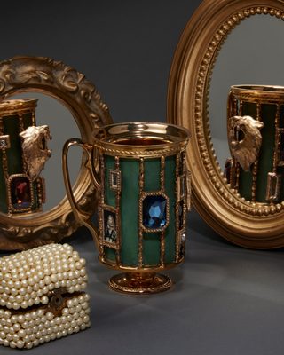 緑の七宝風の胴に金の縦の枠が並ぶマグ。青い大きな宝石と肖像画の額。金の鏡に背面が映る