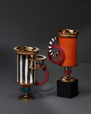 黒白の縦縞の円筒の器と、橙のつや消しの円筒の器。金の縄の口と金の足
