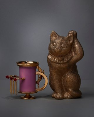 舵輪のような金の取っ手を付けた、紫がかったピンクの円筒の器。金色の猫の置物と並ぶ